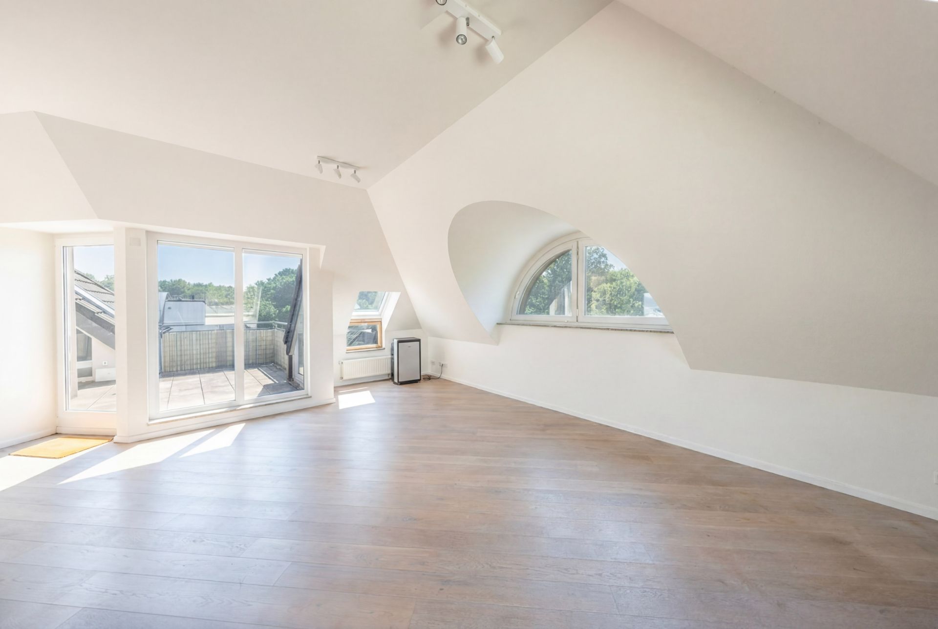 Heller Dachbodenraum mit Holzfußboden, großen Fenstern und Zugang zu einem Balkon.
