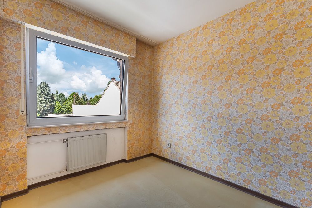 Leerer Raum mit gelber Blumenmuster-Tapete und großem Fenster mit Blick ins Grüne.