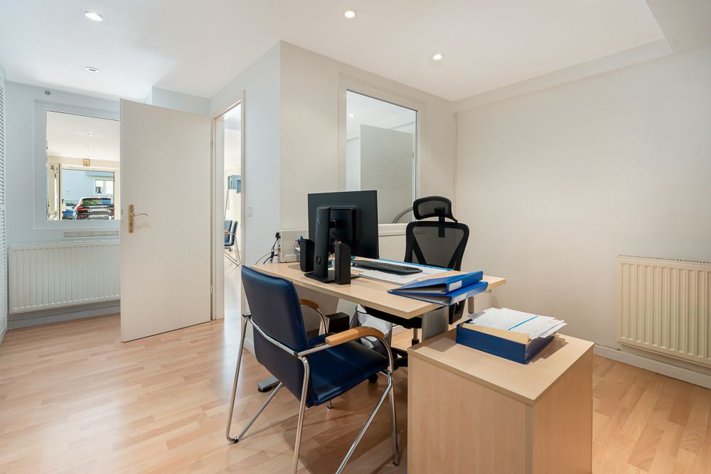 Helles Arbeitszimmer mit Schreibtisch, zwei Stühlen, Computer und Aktenordnern auf Parkettboden.