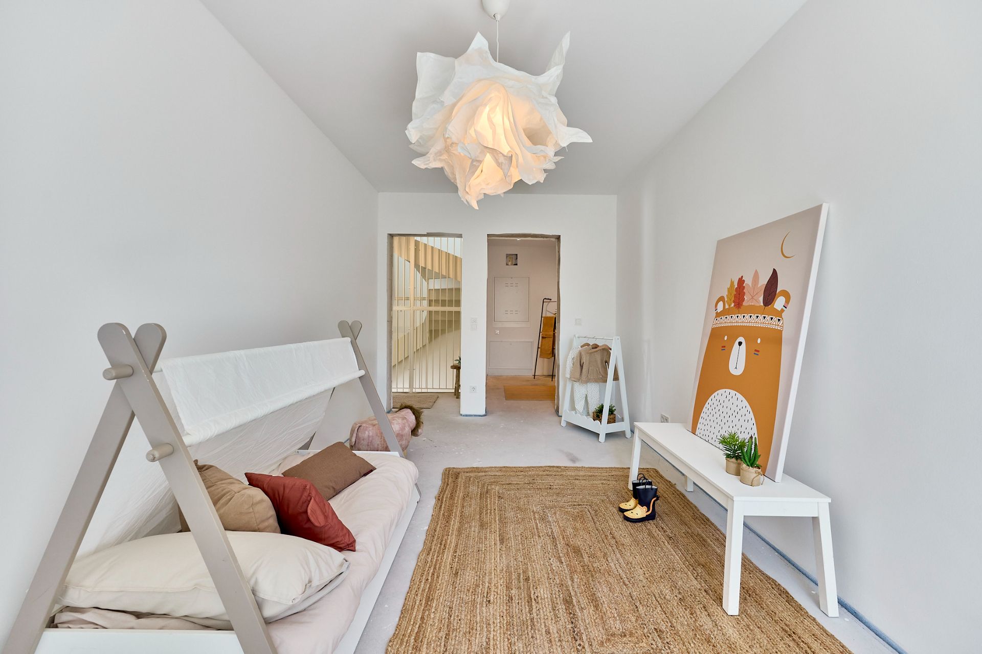 Helles Kinderzimmer mit Bett, Teppich, Tisch, Wandbild und moderner Lampe.
