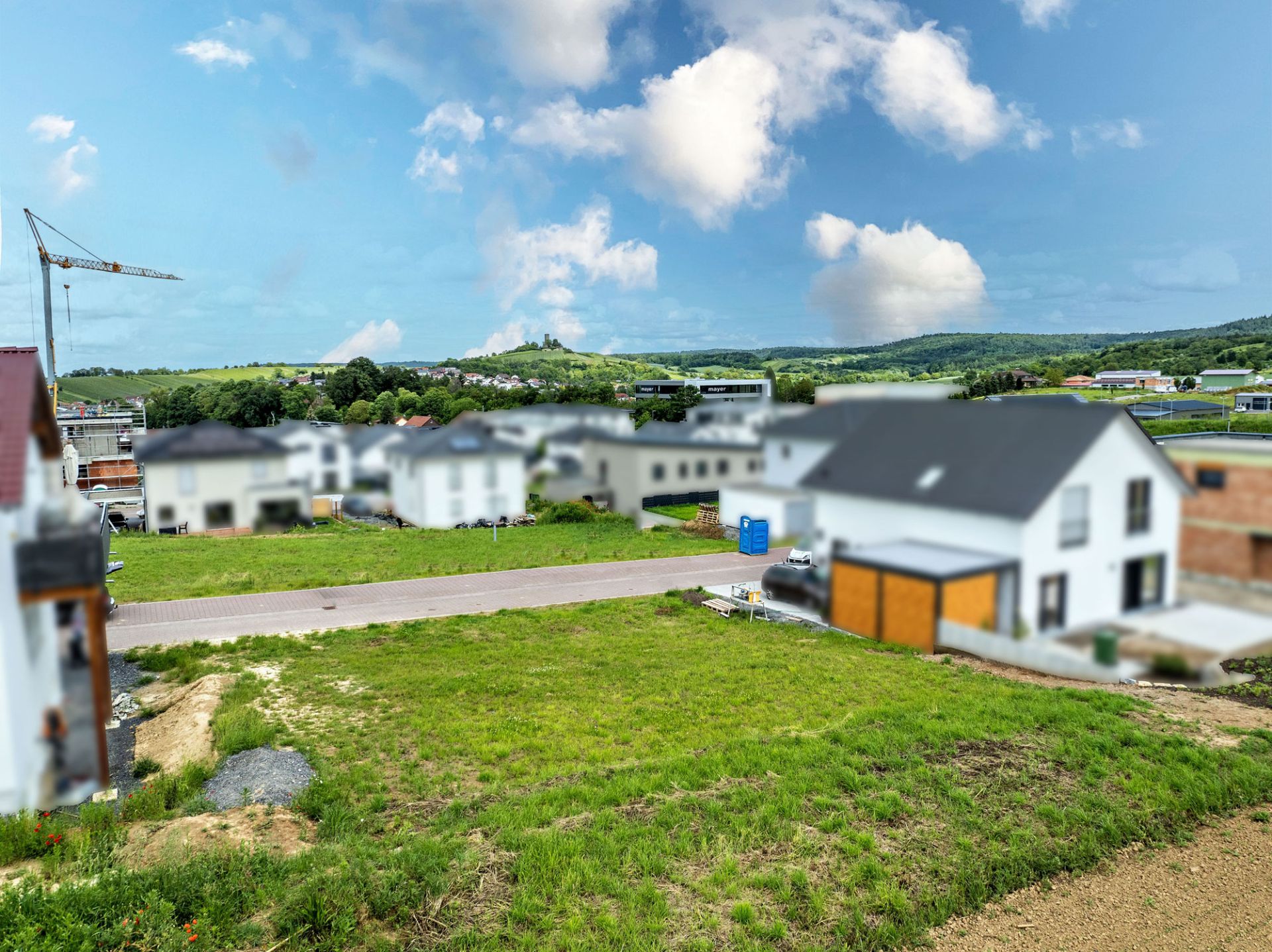 Grünes Grundstück in einem Wohngebiet mit Häusern und Straße im Hintergrund.