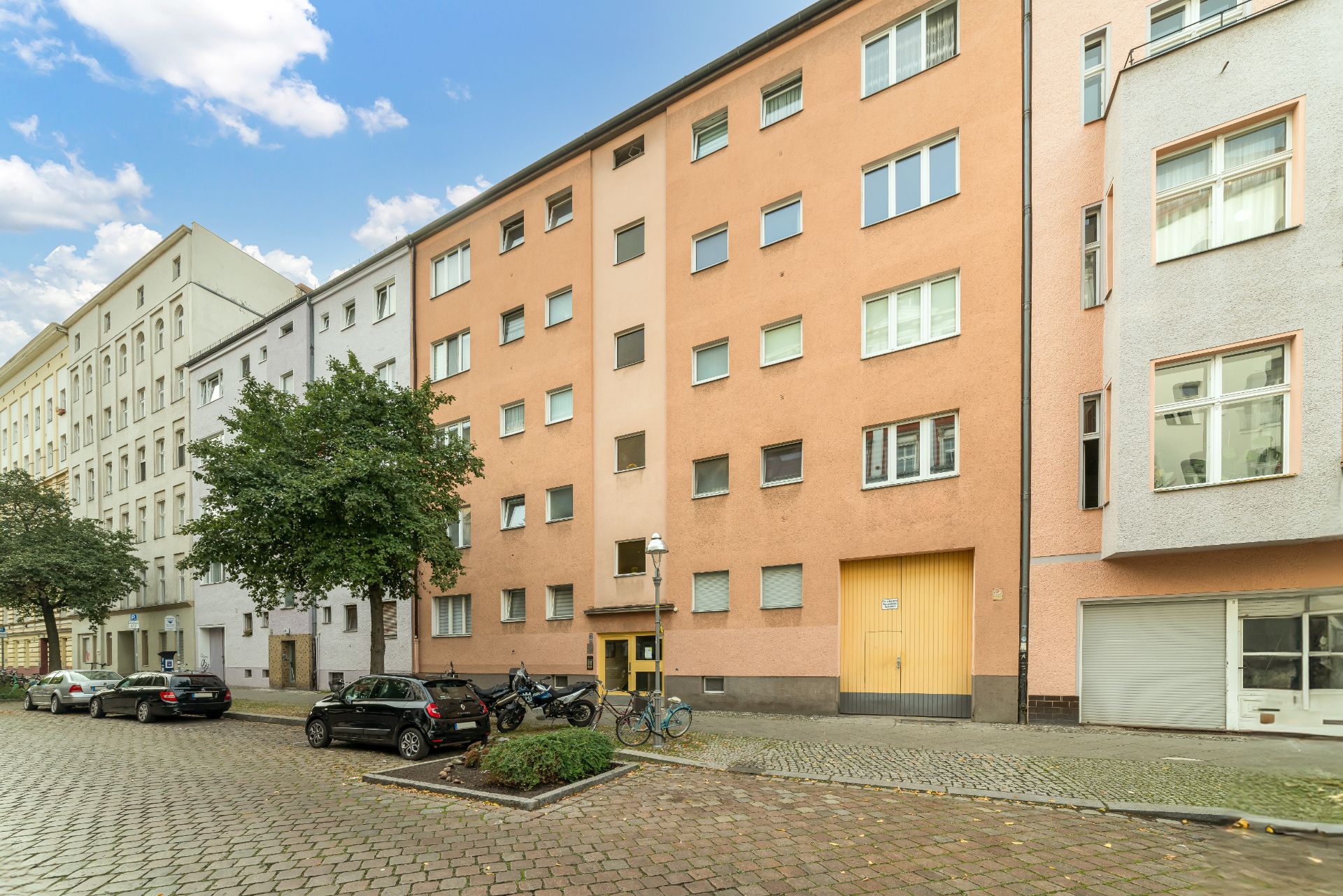 Mehrstöckiges Wohnhaus mit orangefarbener Fassade und mehreren Fenstern an einer ruhigen Straße.