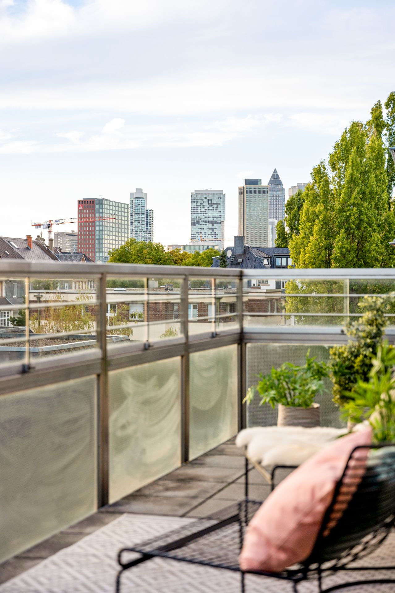 Balkon mit Pflanzen und Stadtblick, im Vordergrund Stuhl mit Kissen und Decke.