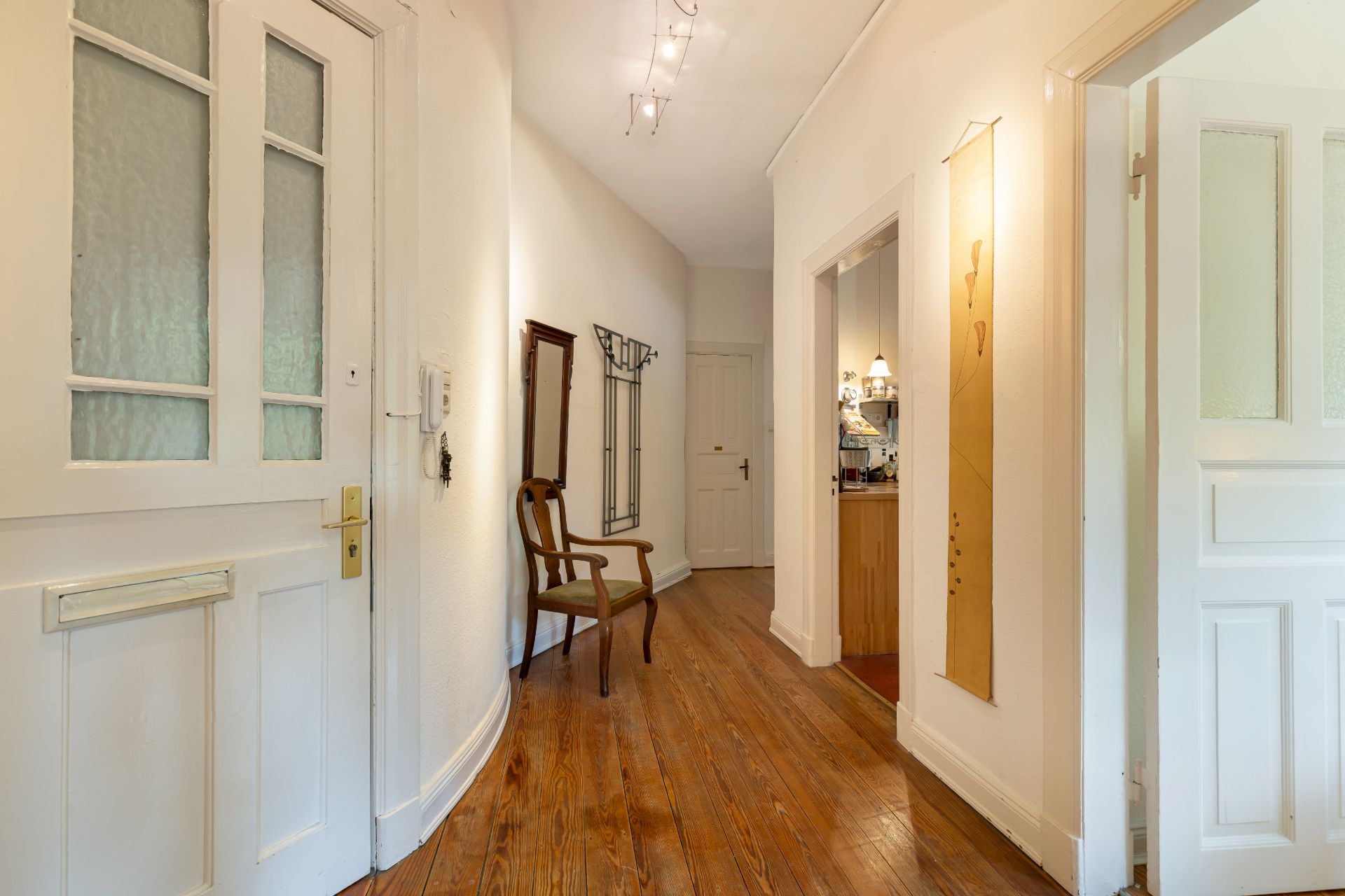 Heller Flur mit Holzboden, Stuhl, Spiegel und Garderobe, Türen führen zu weiteren Räumen.