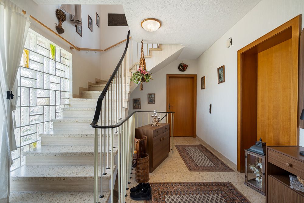 Heller Flur mit offener Treppe, Glasbausteinfenster und Holzmöbeln.