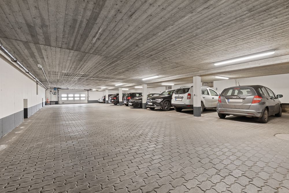 Helle Tiefgarage mit mehreren geparkten Autos und Betonpfeilern.