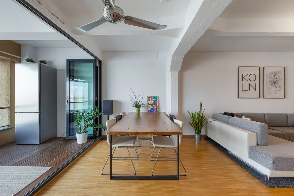 Essbereich mit Holztisch, Stühlen, Pflanzen und angrenzendem Wohnzimmer mit Sofa.