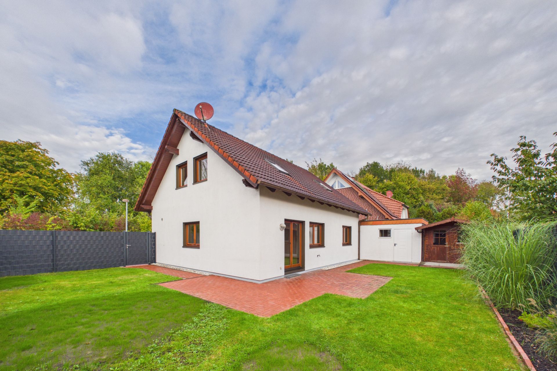 Weißes Einfamilienhaus mit rotem Dach und Garten, umgeben von Rasen und Bäumen.