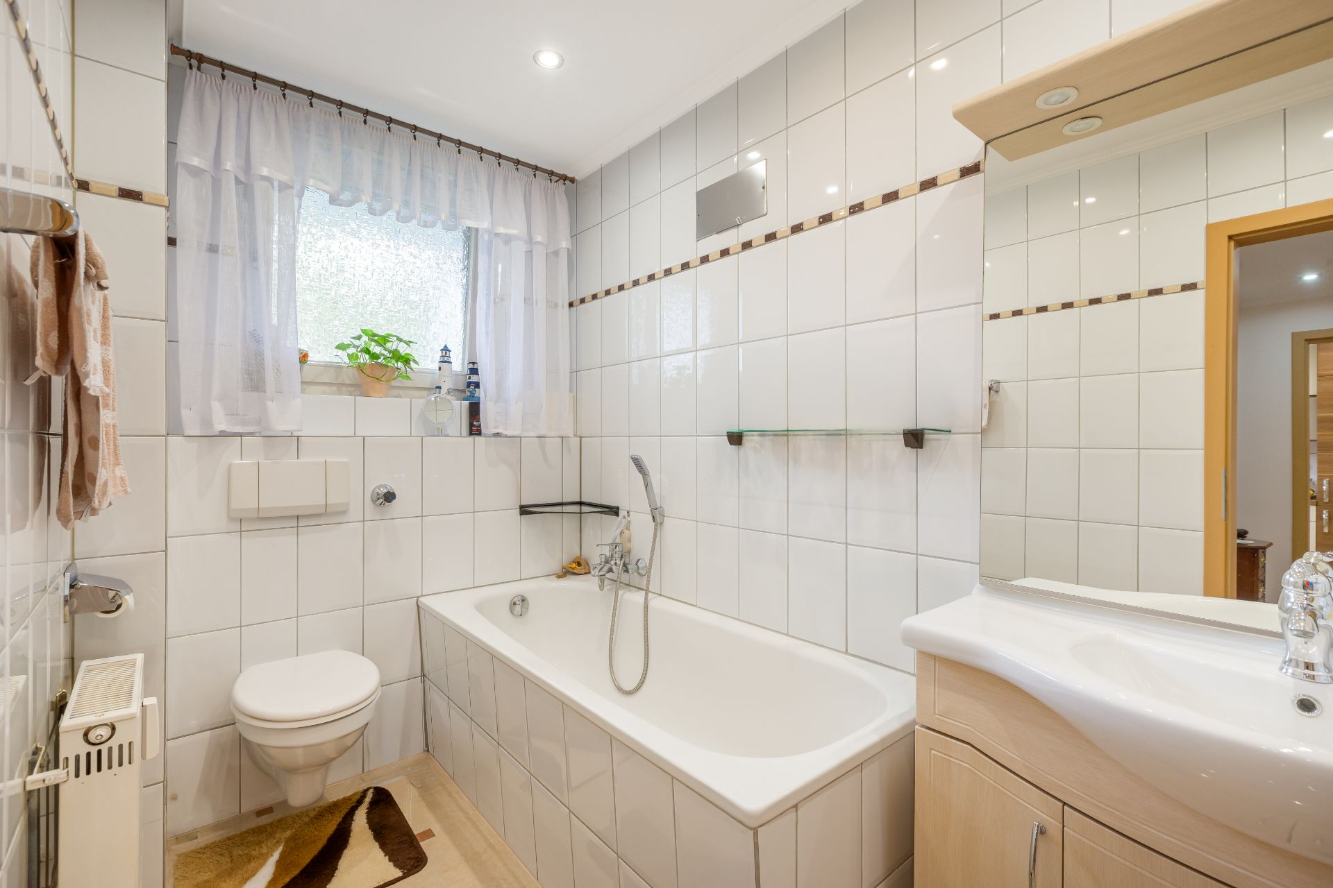 Modernes Badezimmer mit Badewanne, Waschbecken, WC und Fenster mit Vorhang.