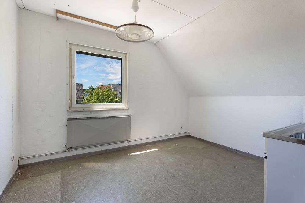 Leeres Zimmer mit einem Fenster, Heizkörper und Deckenlampe, im rechten Bereich eine Arbeitsplatte.