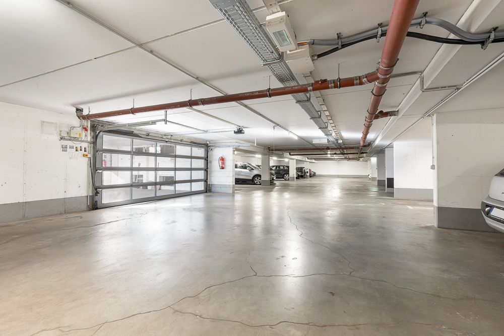 Helle Tiefgarage mit geparkten Autos und großen Rohren an der Decke.