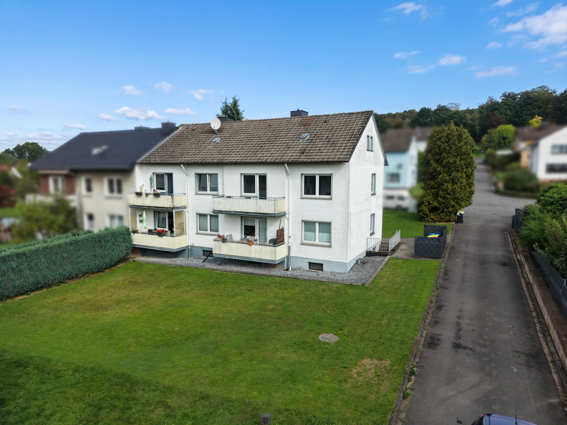 Zweistöckiges Wohnhaus mit Balkonen, großem Garten und Einfahrt bei Tageslicht.
