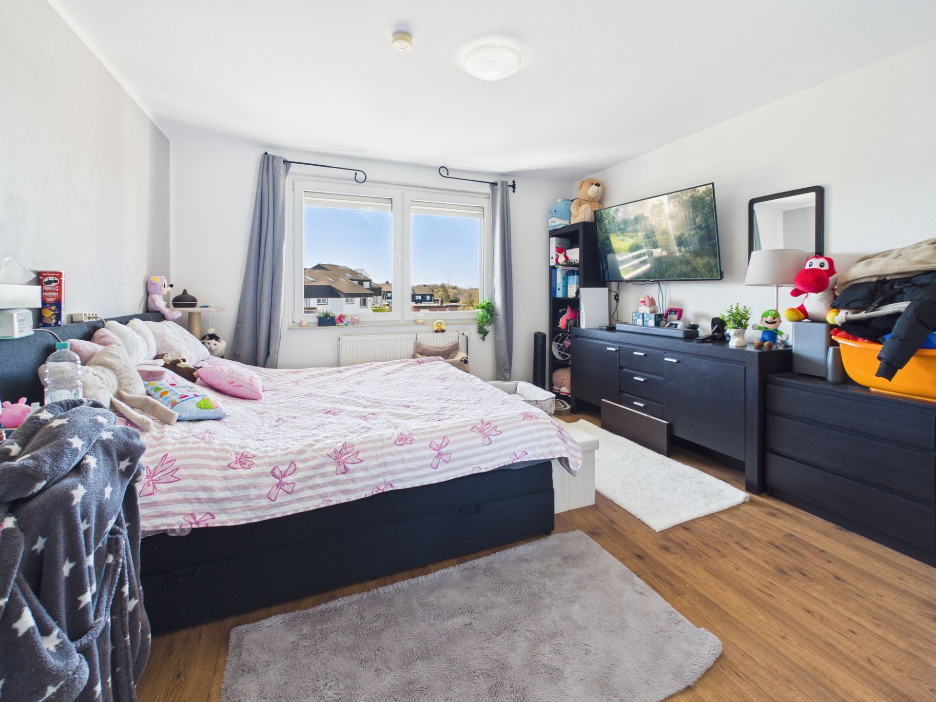 Helles Schlafzimmer mit Doppelbett, zwei Fenstern, Schränken und Holzfußboden.