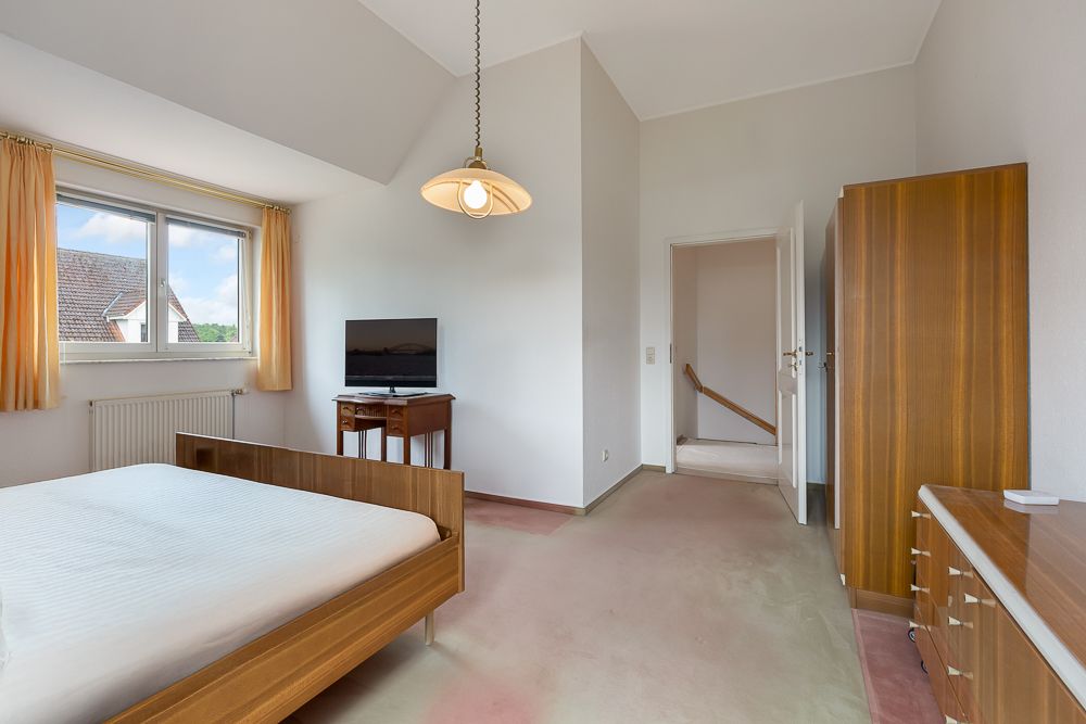 Schlafzimmer mit Holzbett, Schrank, Kommode, Fernseher und Fenster mit gelben Vorhängen.