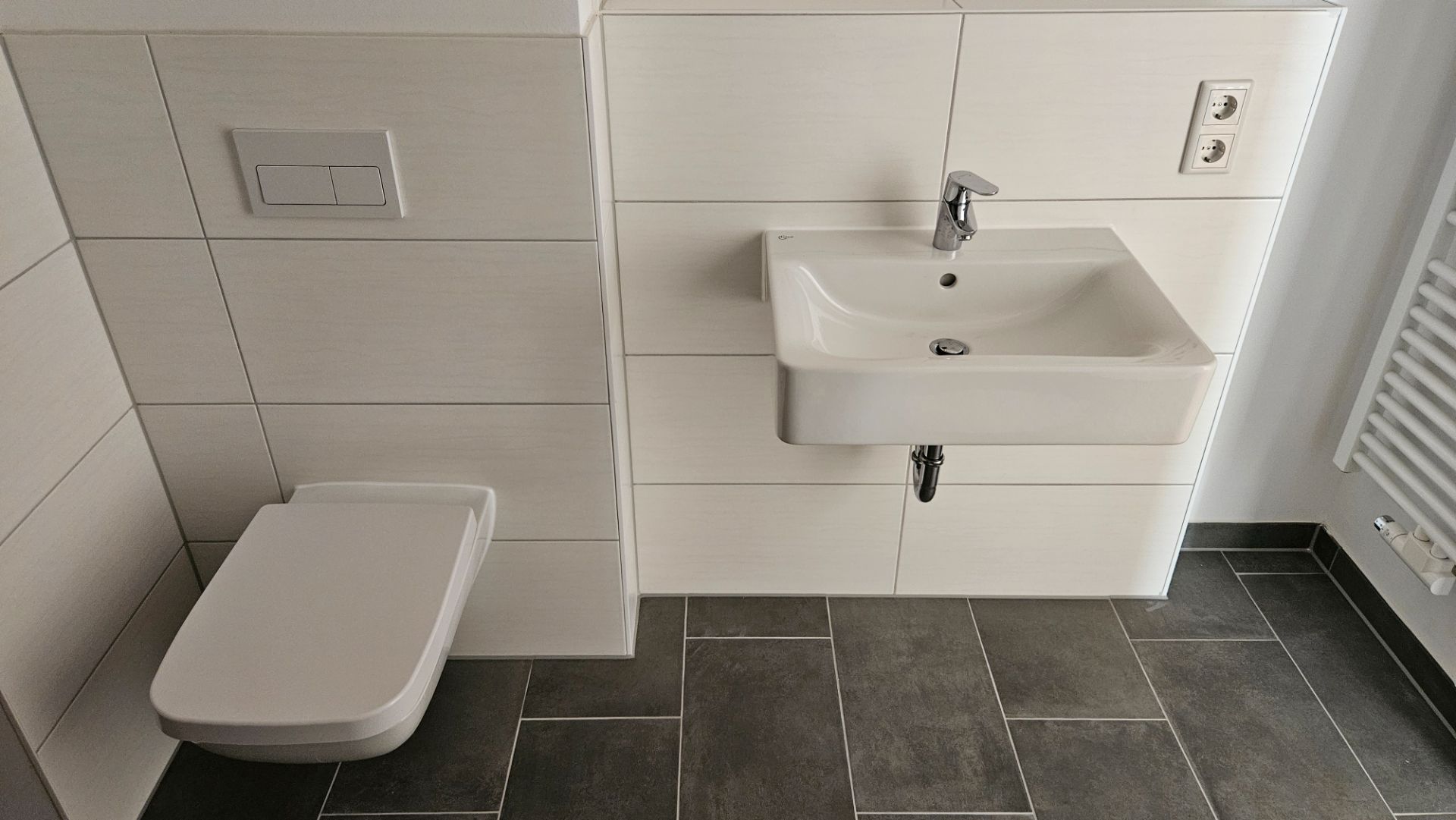Modernes Badezimmer mit Wandtoilette, Waschbecken und Handtuchheizkörper.