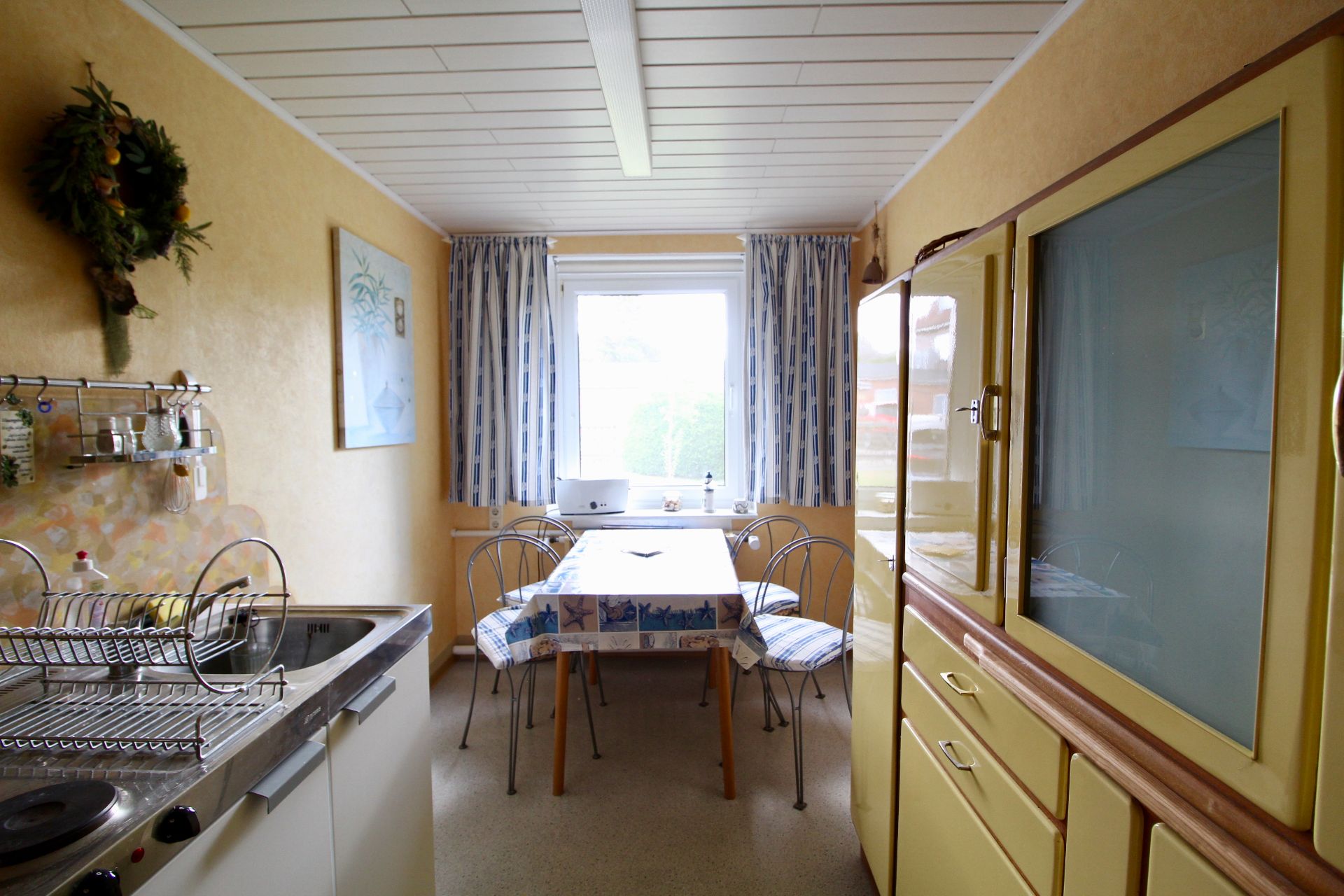 Küche mit gelben Schränken, Esstisch und vier Stühlen vor einem Fenster mit Vorhängen.