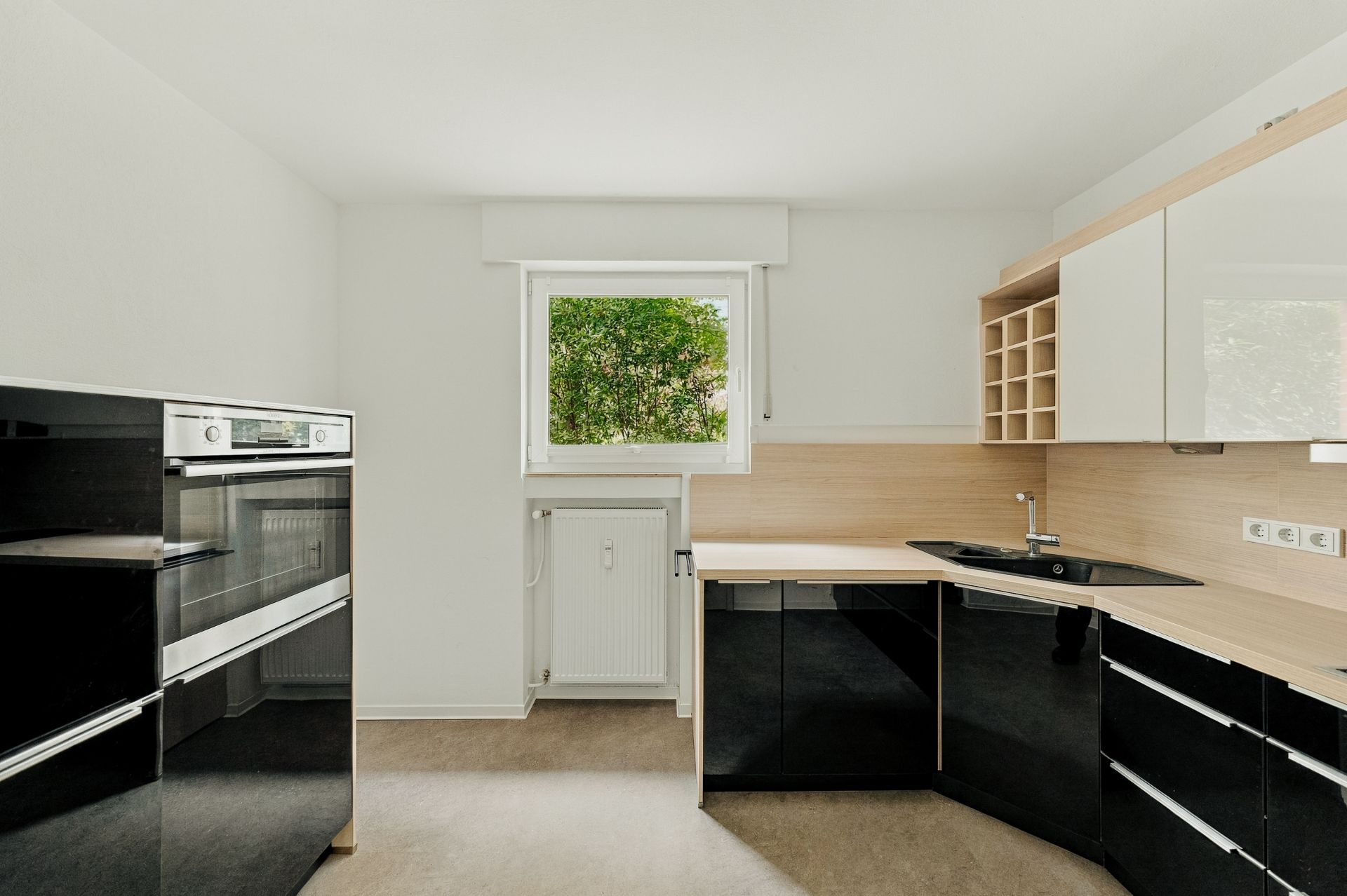 Moderne Einbauküche mit schwarzen Unterschränken, weißen Oberschränken und Fenster mit Blick ins Grüne.
