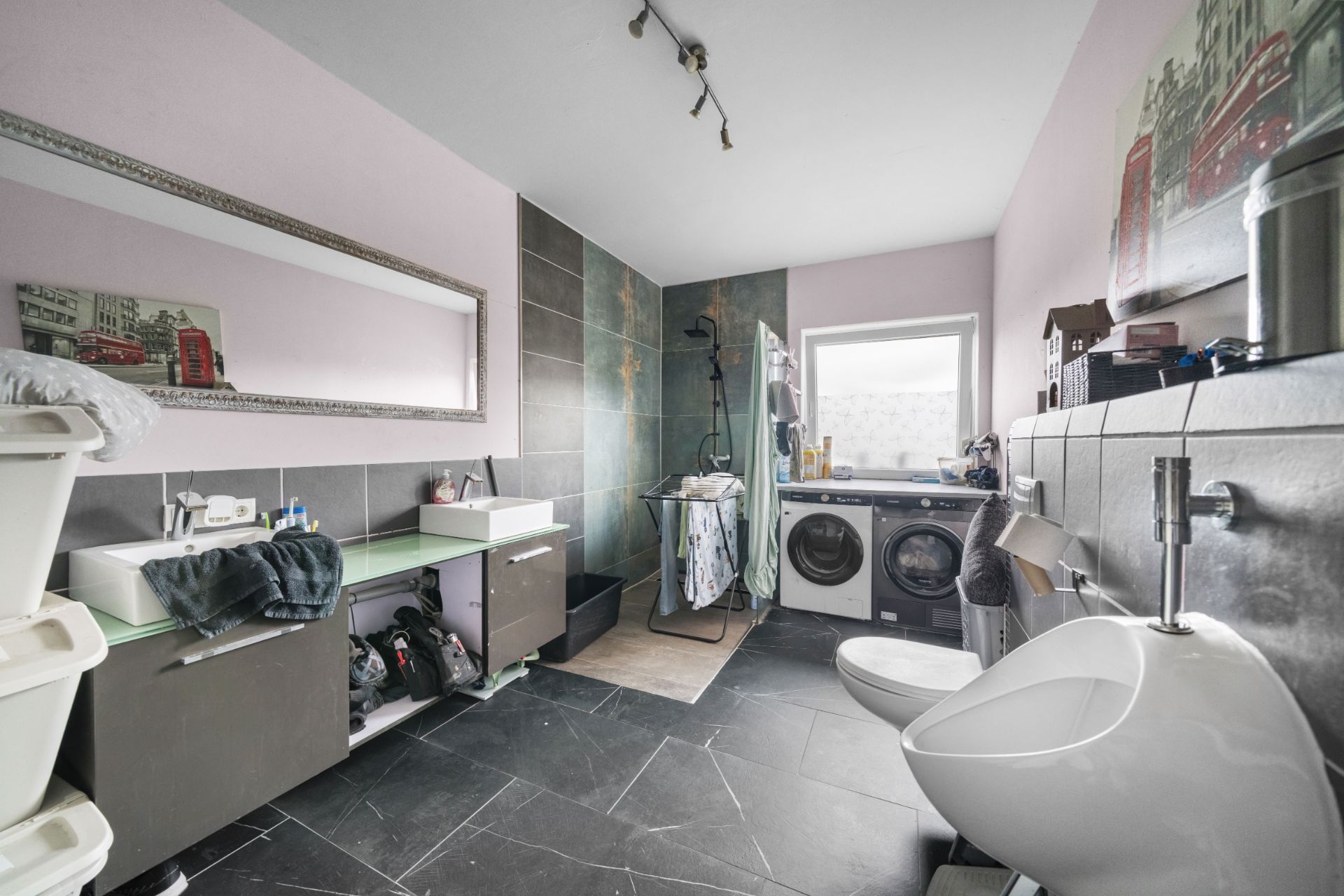 Modernes Badezimmer mit zwei Waschbecken, Dusche, Urinal, Waschmaschine und großem Spiegel.