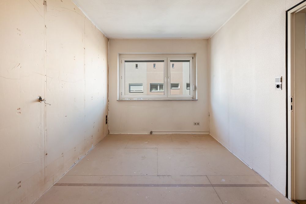 Leerer Raum mit beigen Wänden, Fenster und hellem Boden, keine Möbel vorhanden.