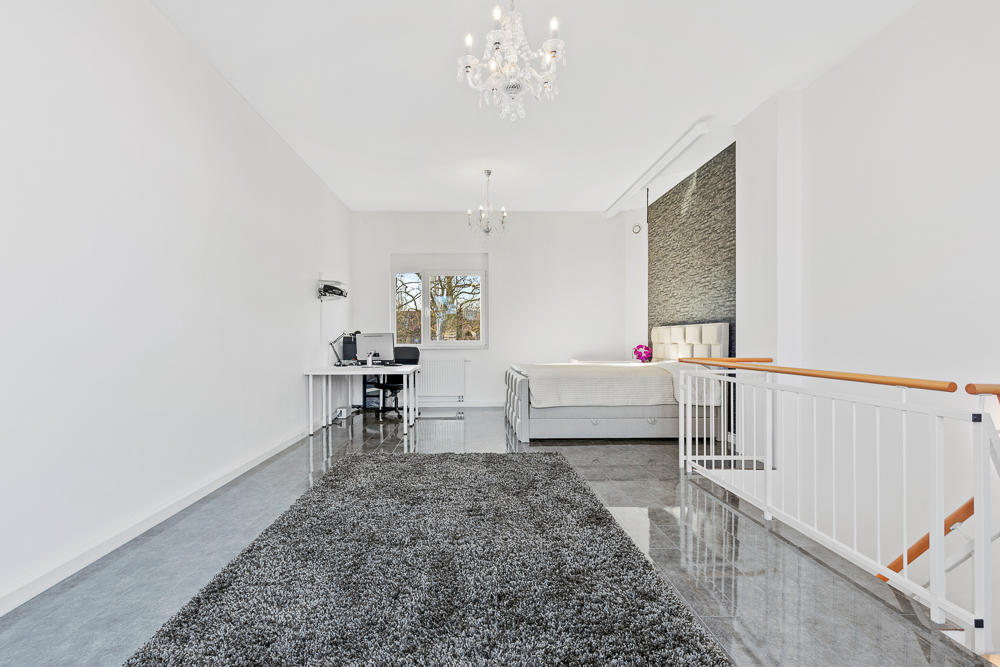 Helles Schlafzimmer mit Bett, Schreibtisch, grauem Teppich und Kronleuchtern.