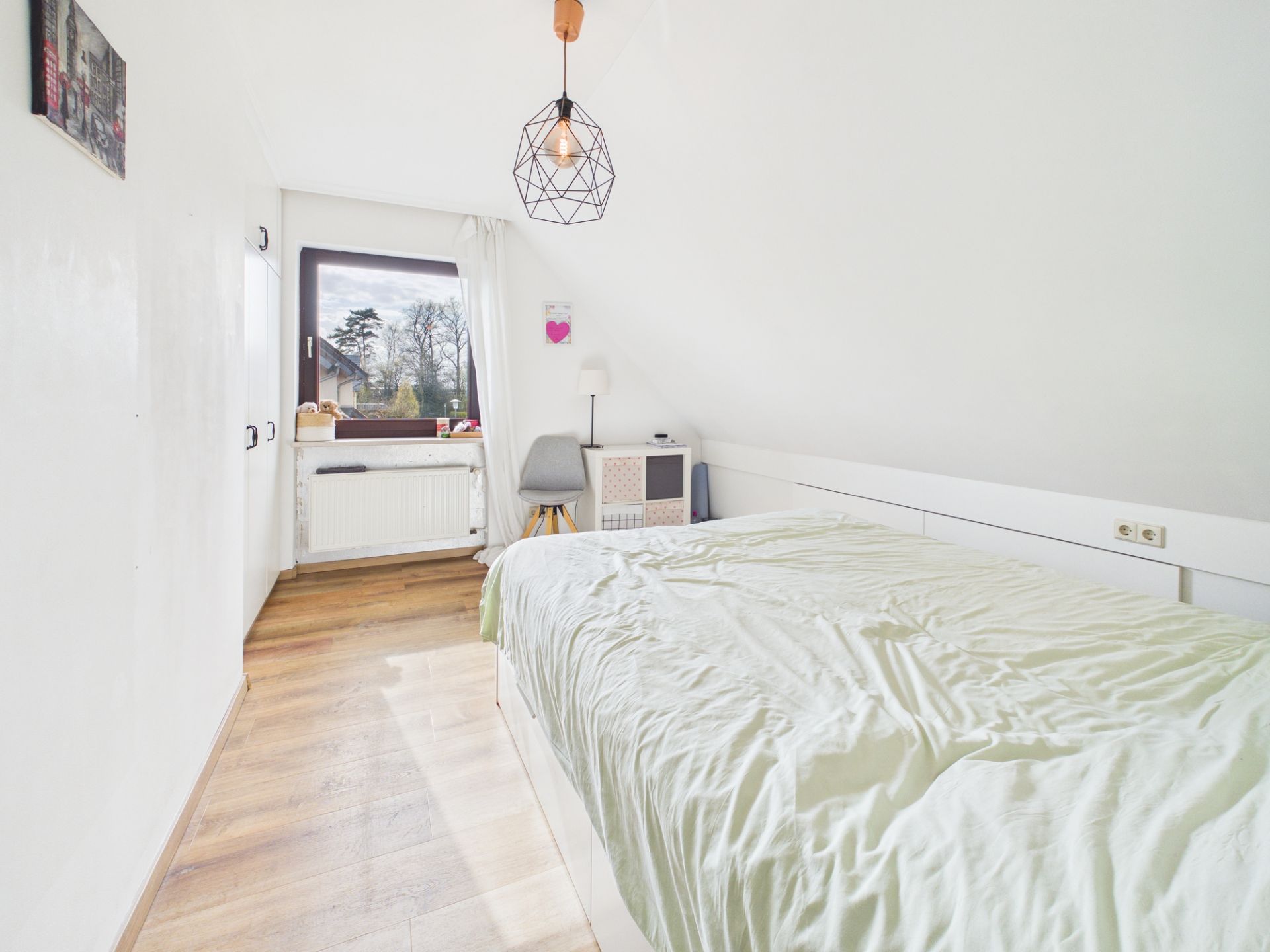 Helles Schlafzimmer mit Holzfußboden, großem Bett, Schreibtisch und Fenster mit Blick nach draußen.
