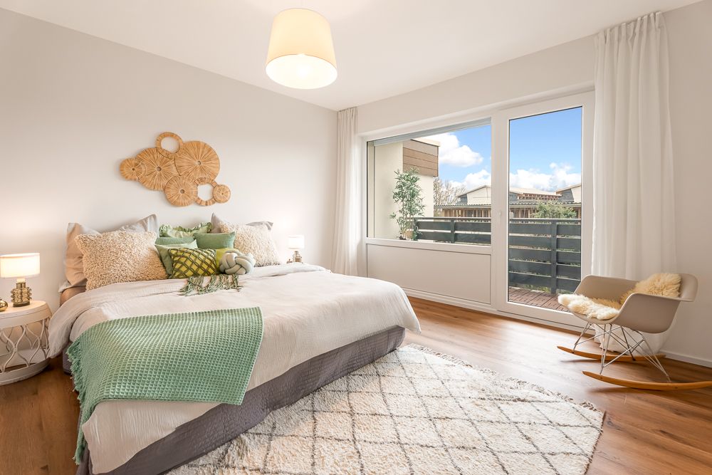 Helles Schlafzimmer mit großem Bett, Schaukelstuhl und Zugang zu einem Balkon.