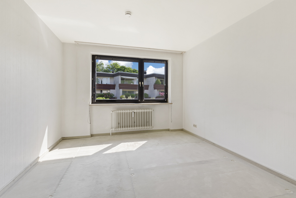 Leerer, heller Raum mit großem Fenster und Heizkörper, Blick nach draußen.