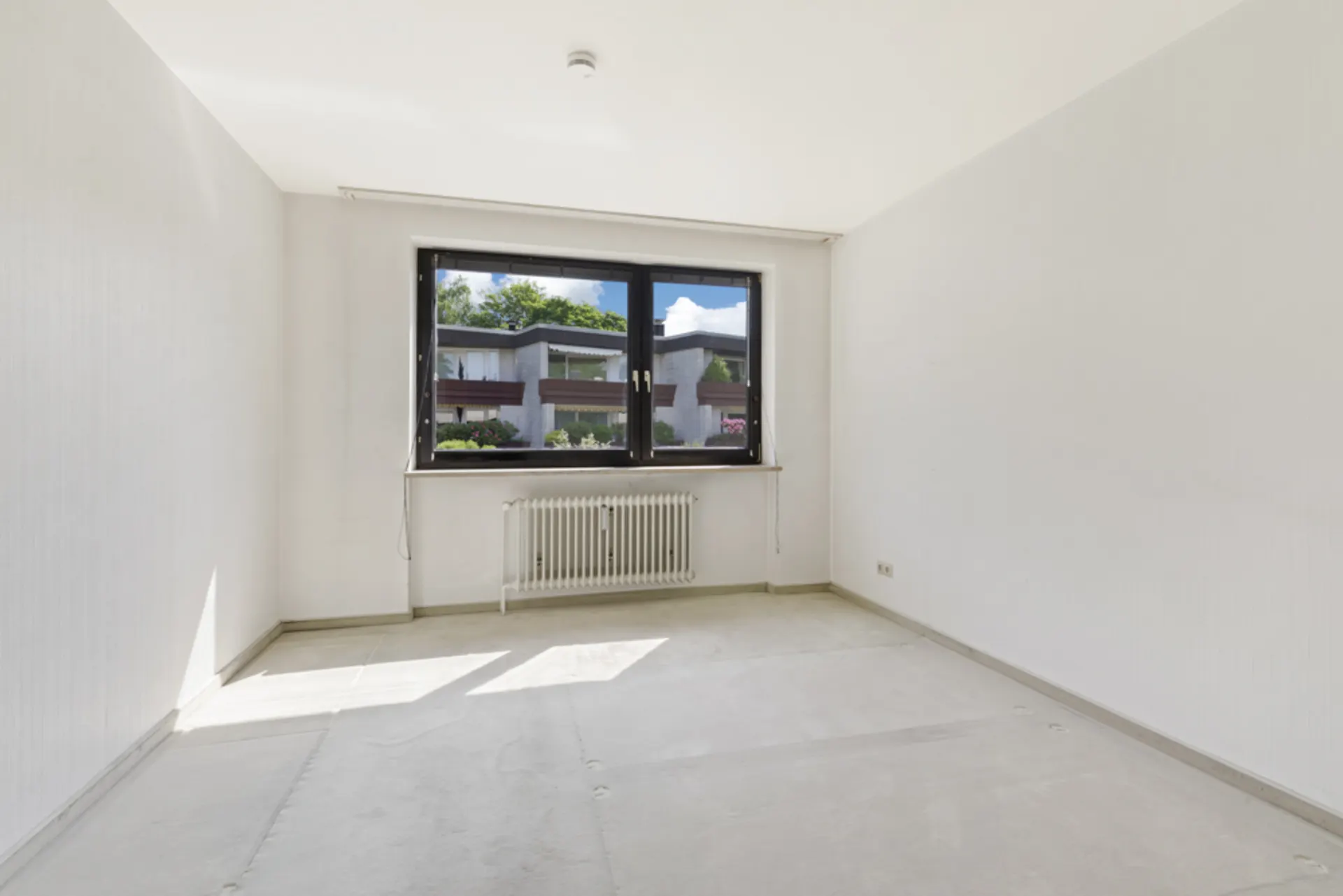 Leerer, heller Raum mit großem Fenster und Heizkörper, Blick nach draußen.
