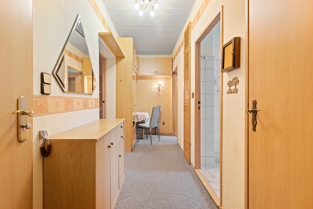 Heller Flur mit Holzschränken, Spiegel, mehreren Türen und Sicht auf einen Essbereich.