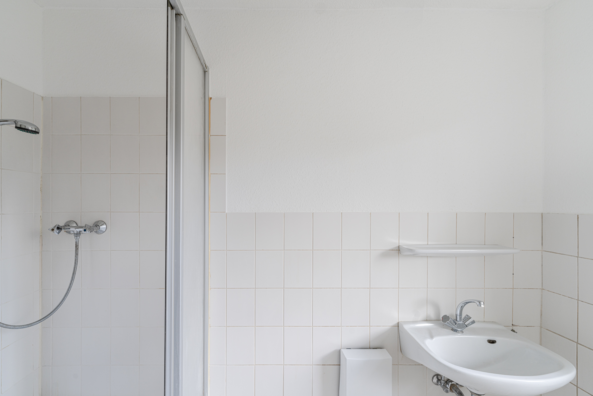 Helles Badezimmer mit Dusche, Waschbecken und Wandregal.