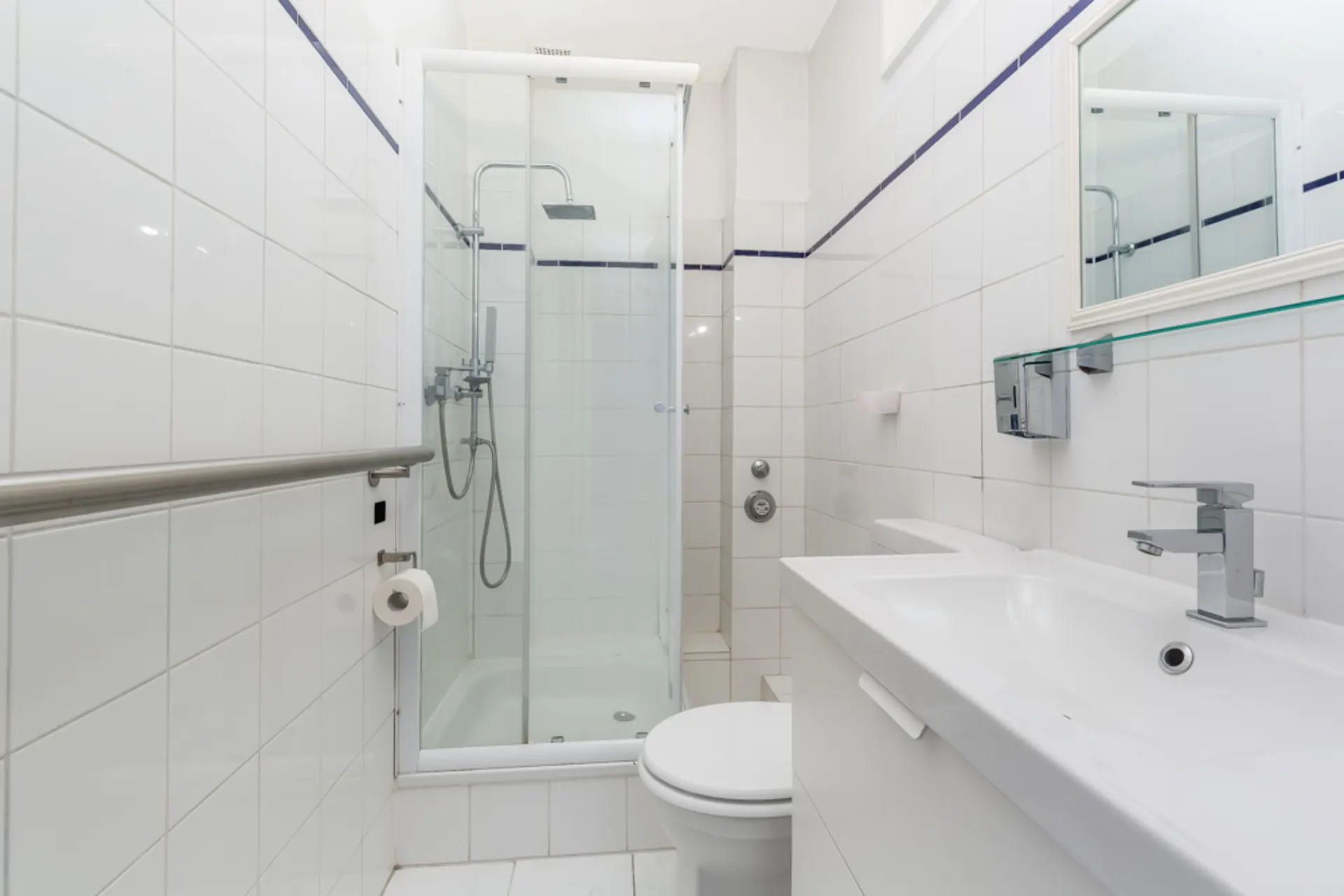 Helles Badezimmer mit Dusche, Waschbecken und Toilette, komplett weiß gefliest.