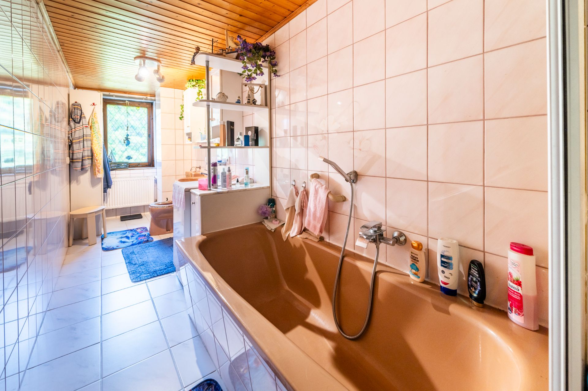 Großes Badezimmer mit brauner Badewanne, Regal, Fenster und weißen Fliesen.
