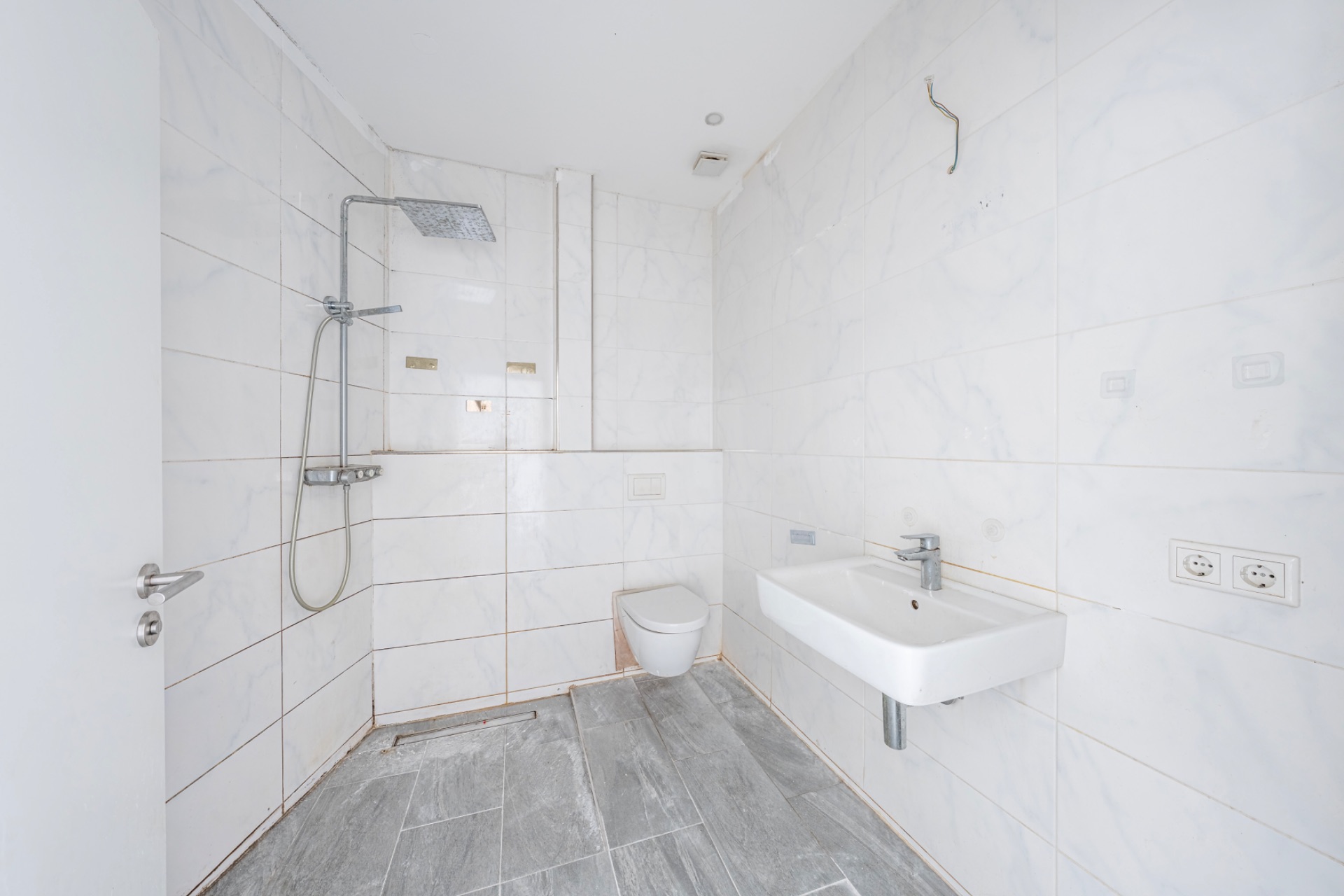 Modernes, weiß gefliestes Bad mit bodengleicher Dusche, Wandwaschbecken und Wandtoilette.