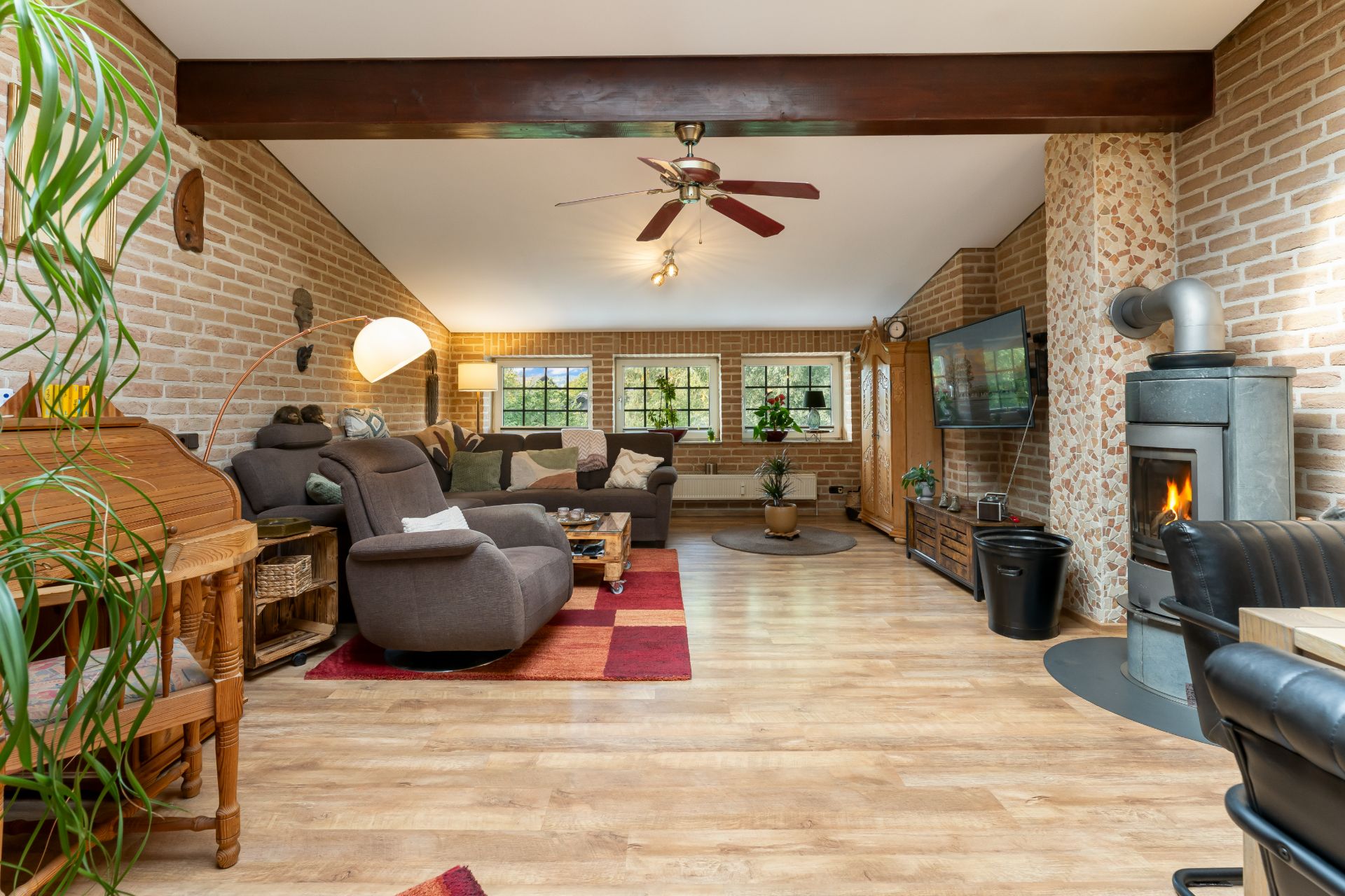 Gemütliches Wohnzimmer mit Holzofen, Sofas, Fernseher und hellen Holzböden.