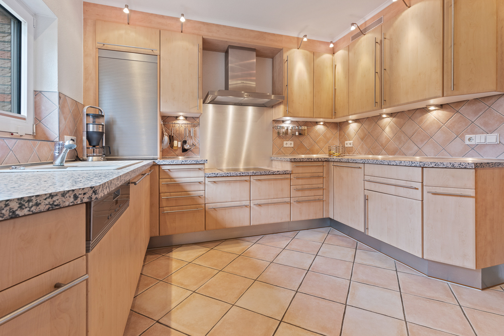 Moderne Einbauküche mit Holzfronten, Granit-Arbeitsplatten und Fliesenboden.