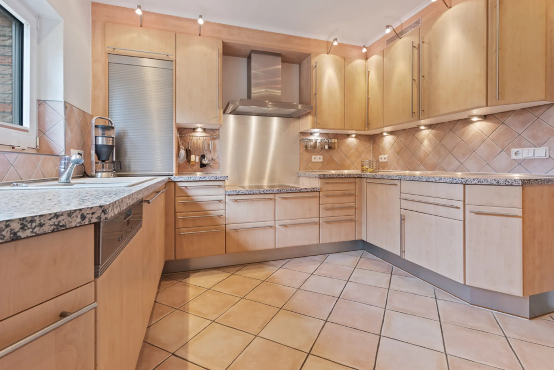 Moderne Einbauküche mit Holzfronten, Granit-Arbeitsplatten und Fliesenboden.