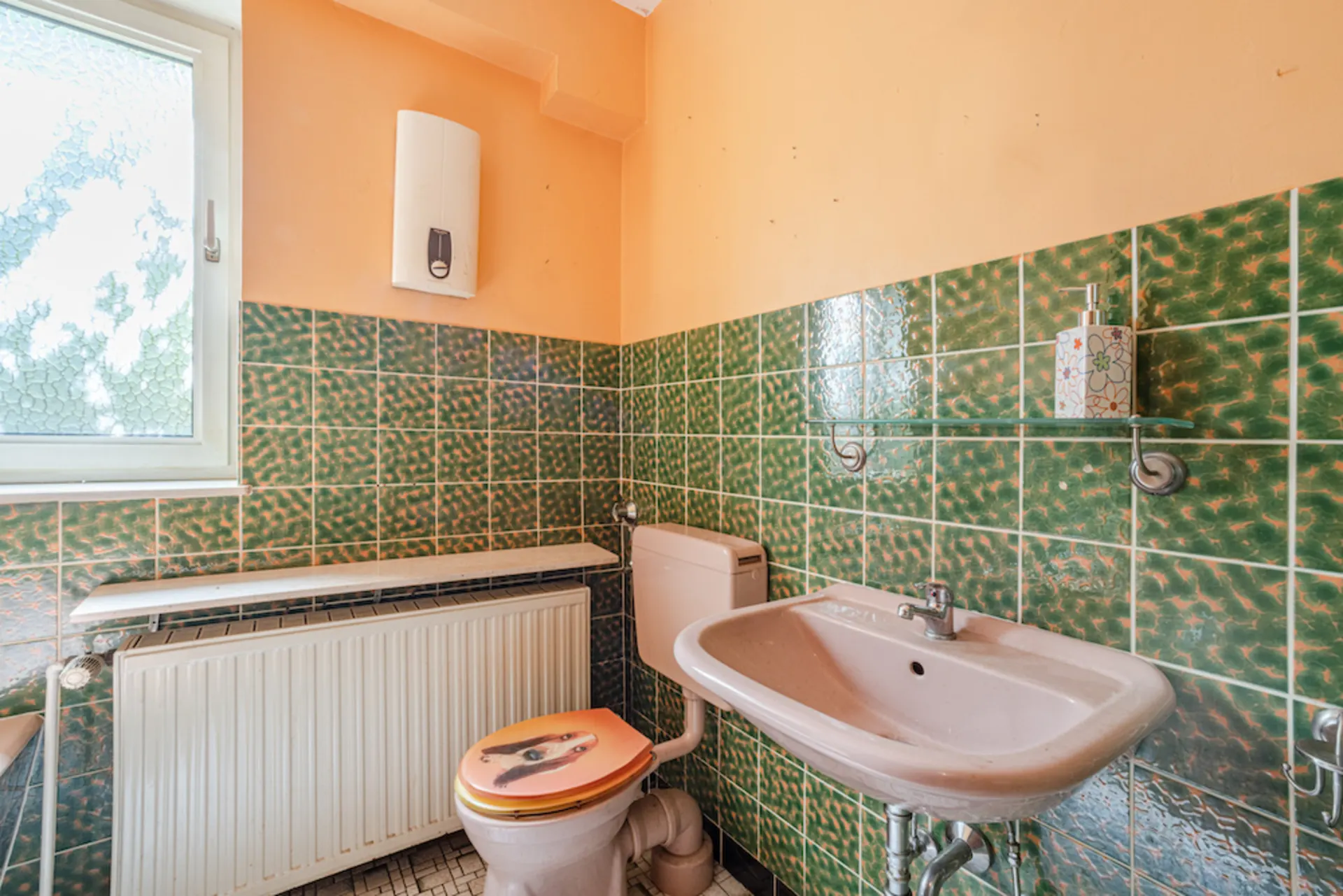 Kleines Bad mit grün gekachelten Wänden, Waschbecken, Toilette und Fenster.