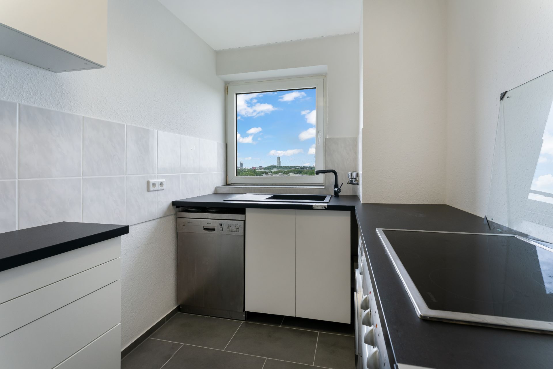 Moderne, schmale Küche mit Herd, Spüle, Geschirrspüler und Fenster mit Blick nach draußen.