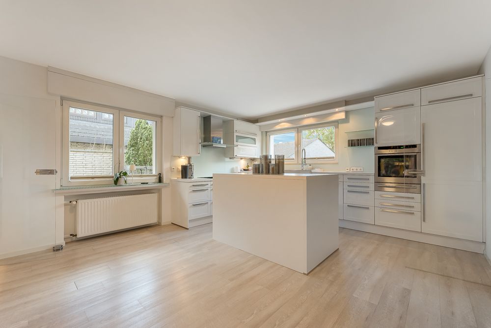Helle, moderne Küche mit Kochinsel, großen Fenstern und Einbaugeräten.