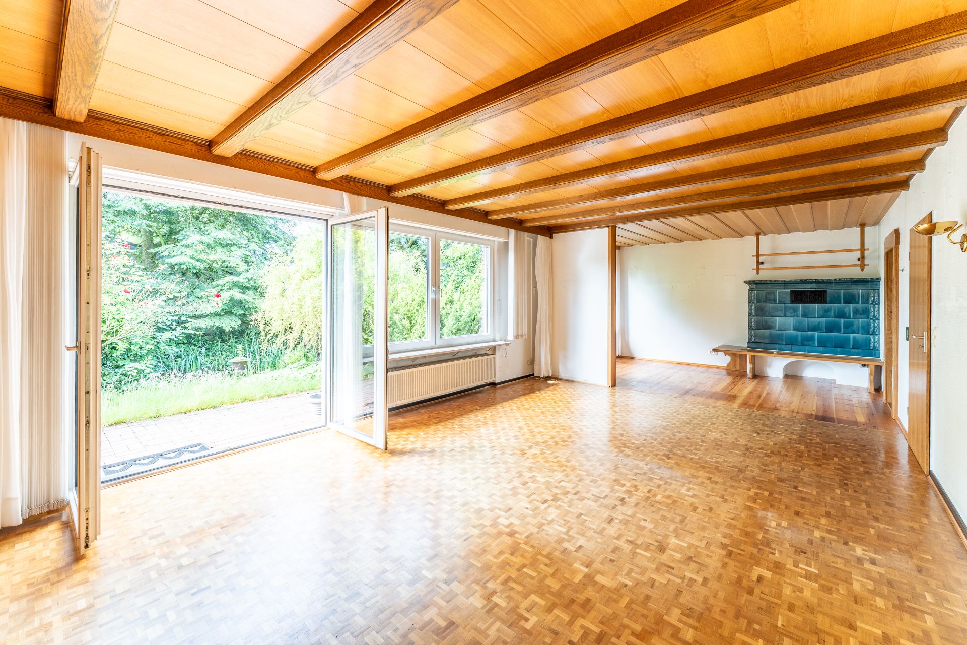 Helles Wohnzimmer mit Parkettboden, Holzdecke, großen Fenstern und offener Tür zum Garten.