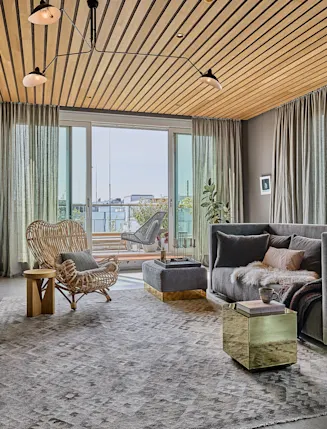 Modernes Wohnzimmer mit Sofa, Sessel, Teppich und großen Fenstern zu einem Balkon.