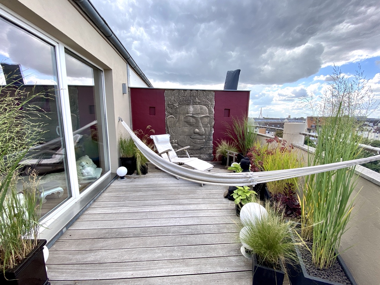 Moderne Dachterrasse mit Hängematte, Pflanzen, Liegestuhl und Wandrelief eines Gesichts.
