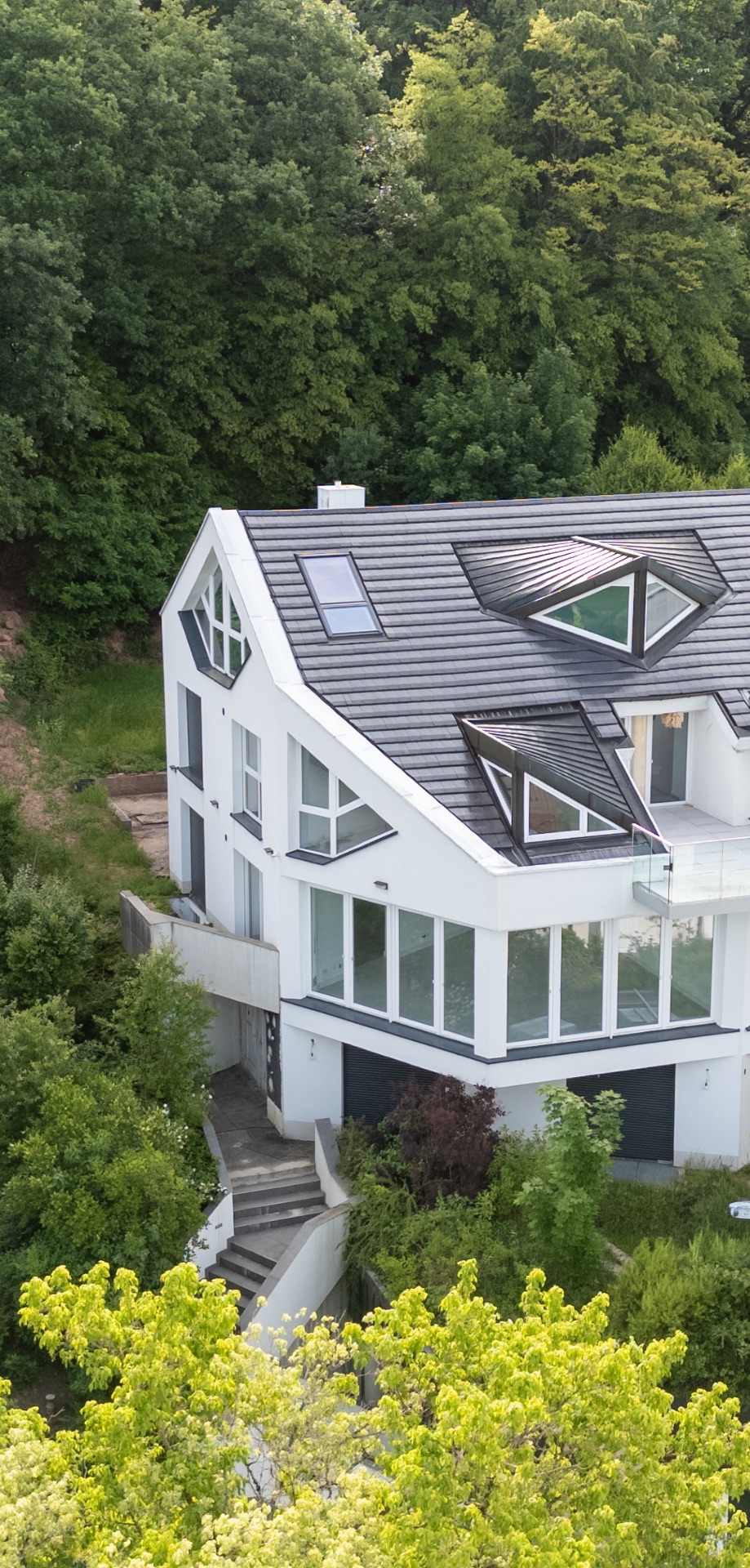 Modernes weißes Wohnhaus mit vielen Fenstern und schrägem Dach, von Bäumen umgeben.