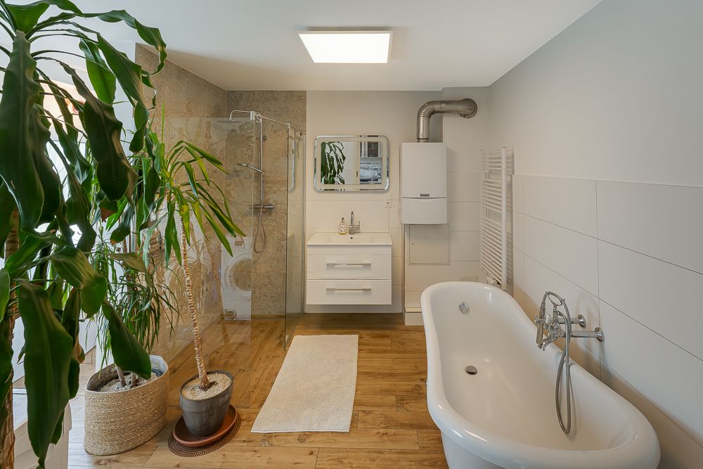 Modernes Badezimmer mit freistehender Badewanne, Dusche, Waschbecken, Pflanzen und Holzfußboden.