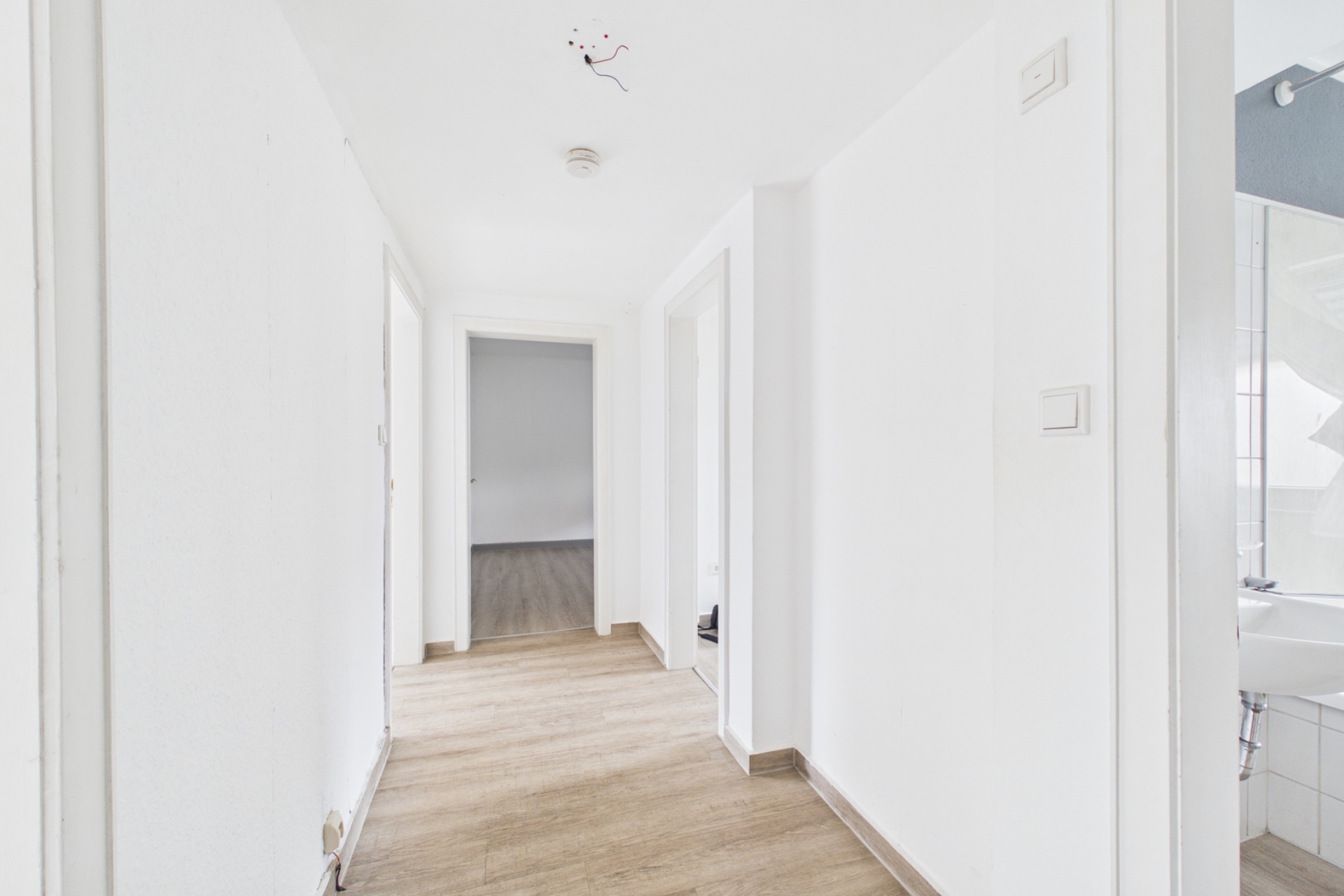 Heller Flur mit Holzboden, mehreren Türen und Blick ins Badezimmer rechts.