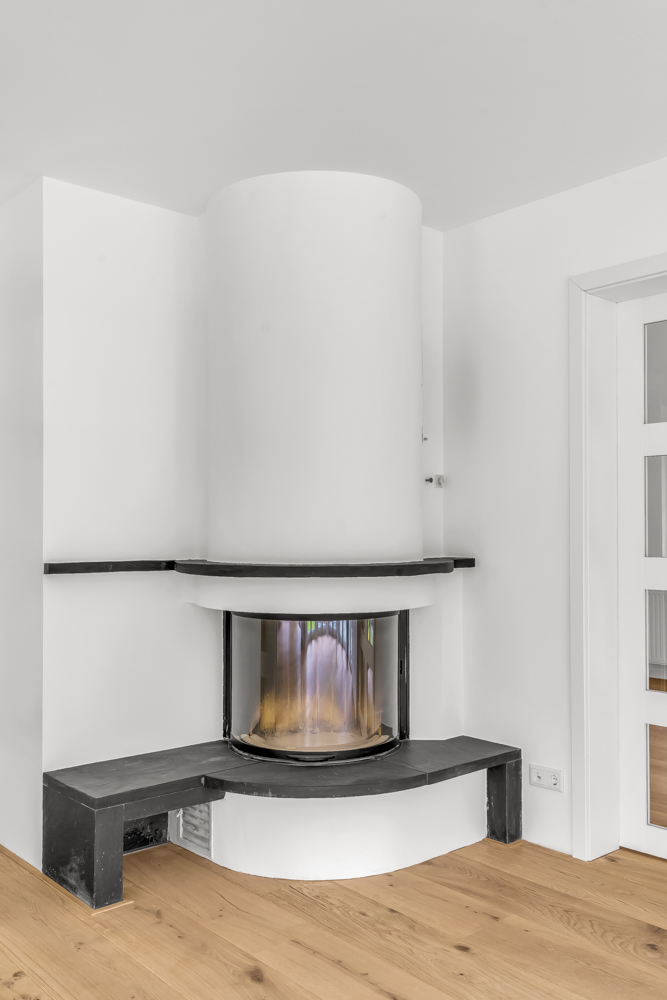 Moderner Kamin mit schwarzer Sitzfläche und Glasfront in einem hellen Raum mit Holzboden.