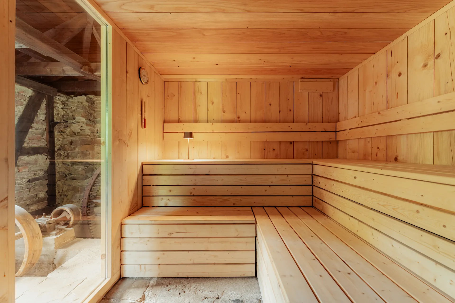 Helle Sauna mit Holzbänken und Fenster, Blick auf eine Steinmauer außen.