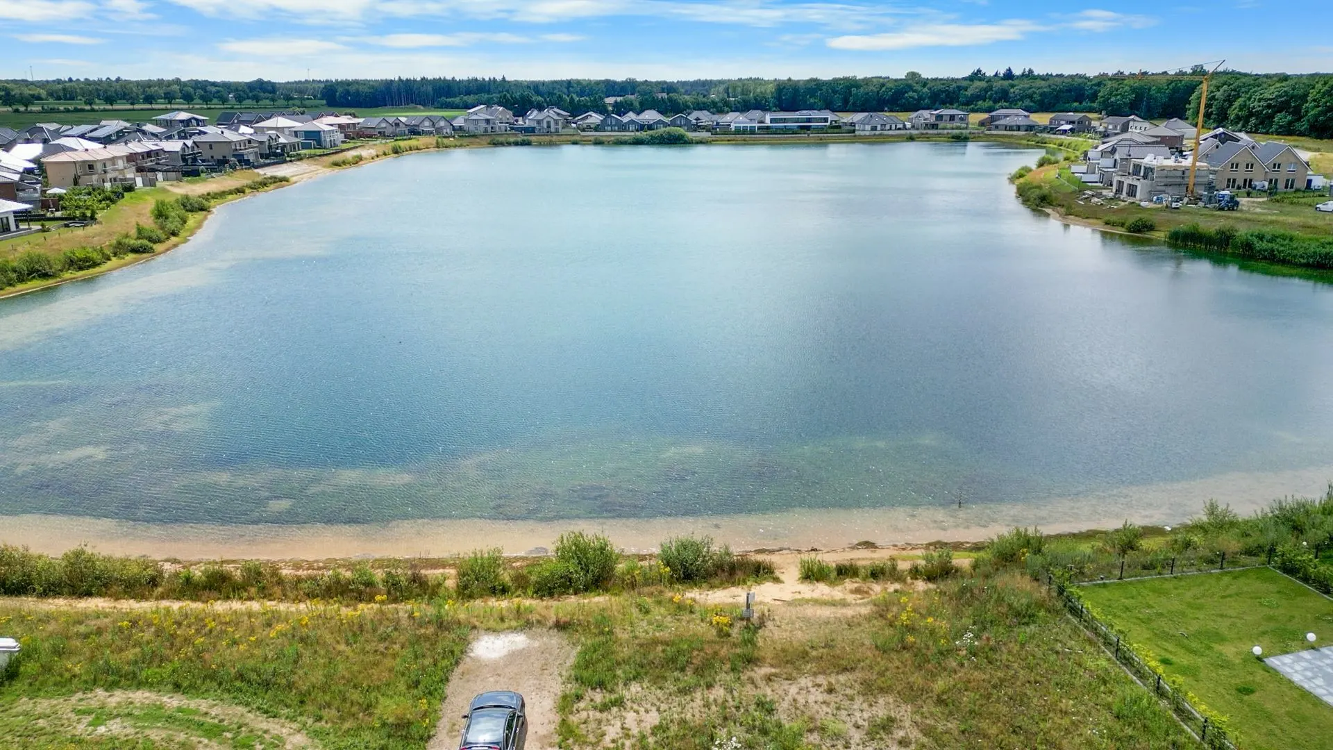 Blick auf einen See mit Häusern am Ufer und einem Auto im Vordergrund.