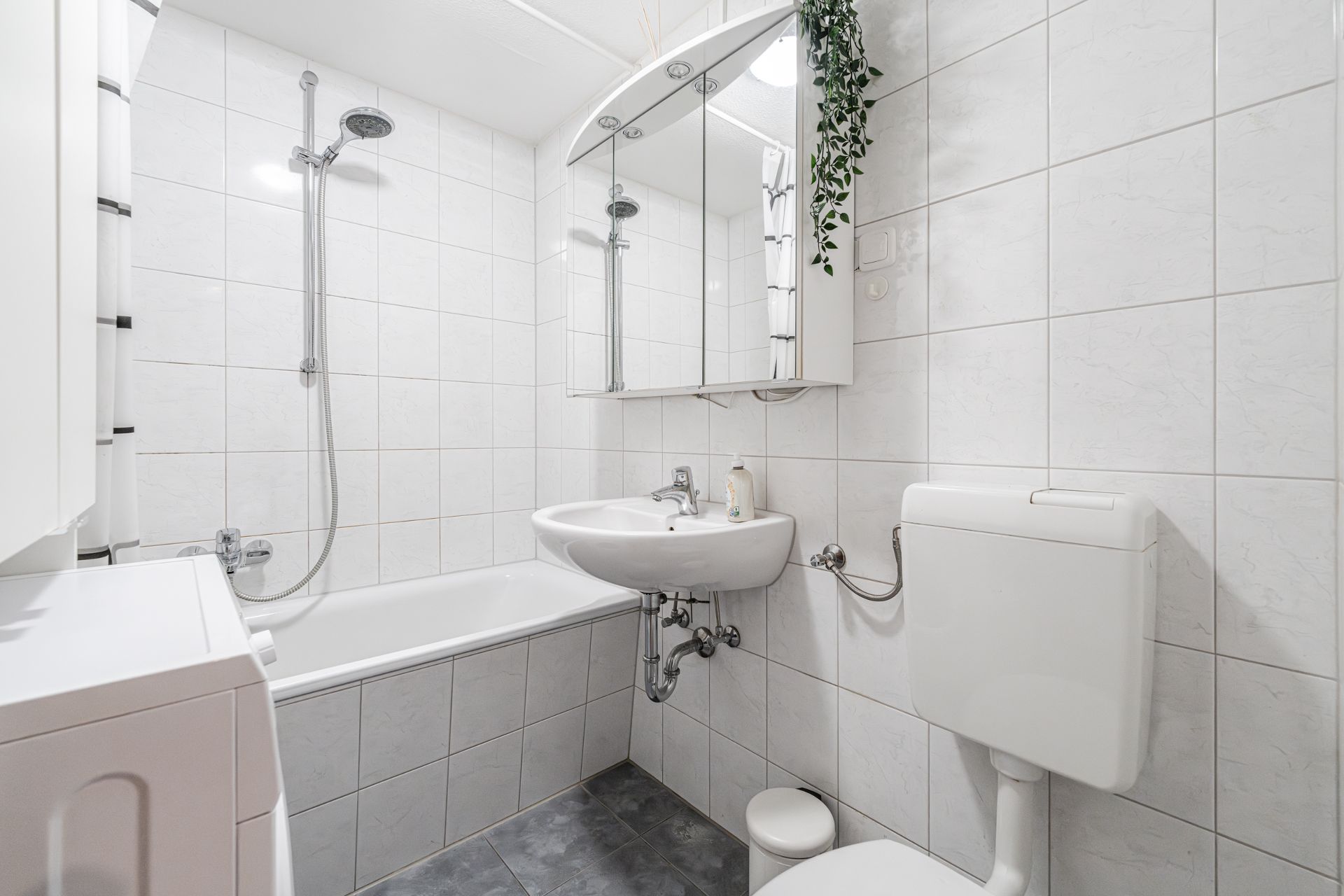 Helles Badezimmer mit Badewanne, Waschbecken, Spiegel, Toilette und Waschmaschine.