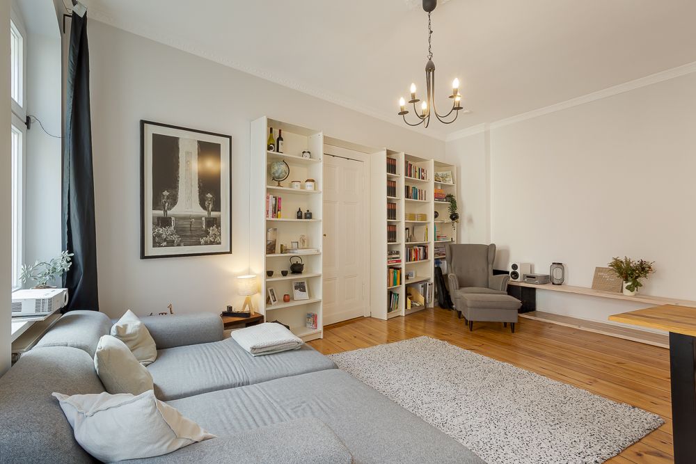Helles Wohnzimmer mit grauem Sofa, Bücherregalen, Teppich und Sessel.